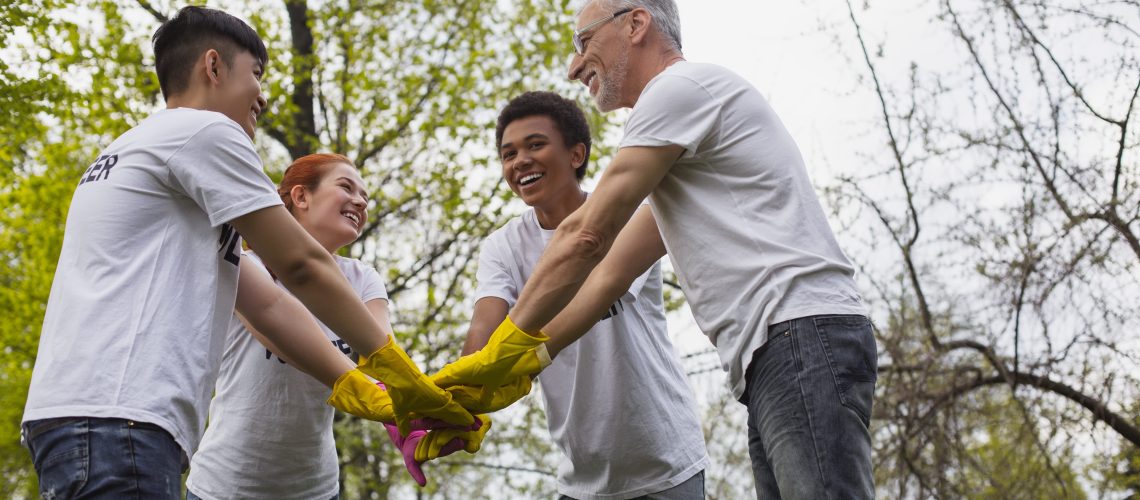 Team spirit. Low angle of optimistic vigorous volunteers standing and holding hands together
